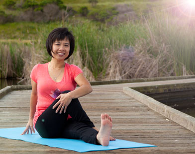 lynn cheng, yoga instructor, in a seated yoga pose, Marichyasana III, outdoors on a wooden plank path